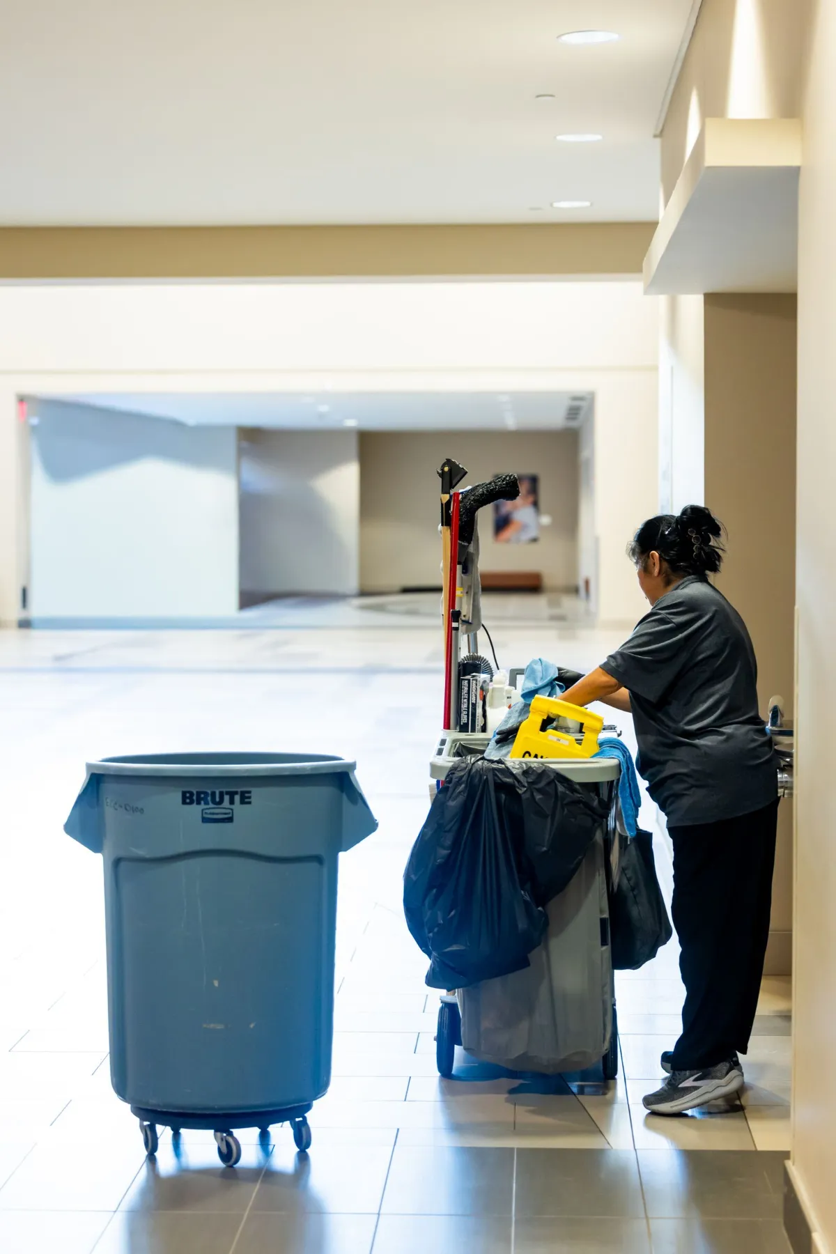 Janitorial cleaner with a cleaning cart and waste bin in a bright open medical facility space in Bentonville, AR