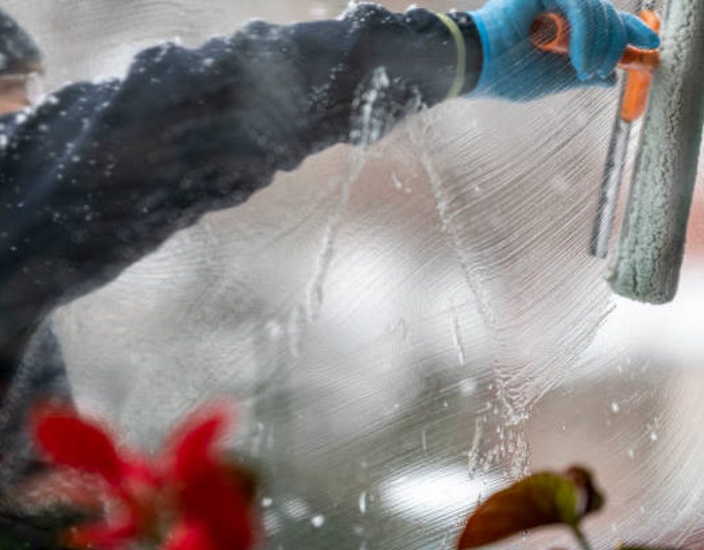 The cleaning worker wipes the window with a rubber squeegee. Cleans a soapy window strip. Cleaning service concept.