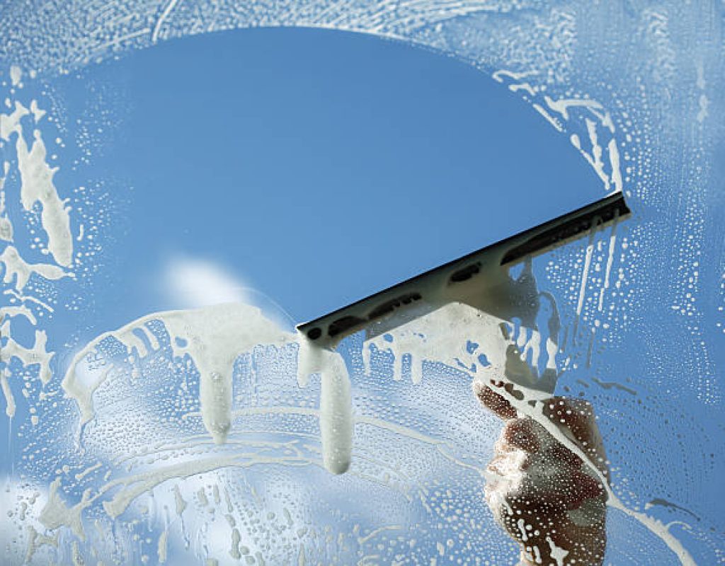 Professional window cleaner inspecting glass for hard water stains in Centerton commercial building