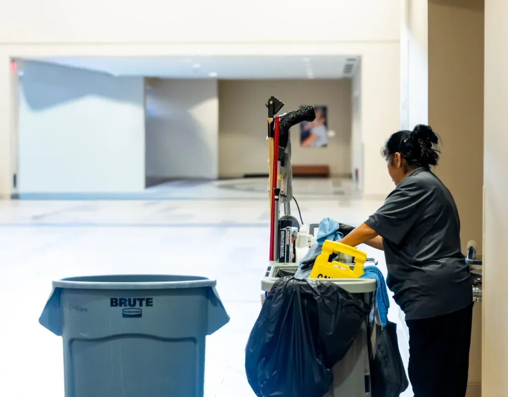 Janitorial cleaner with a cleaning cart and waste bin in a bright open medical facility space in Bentonville, AR